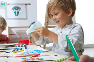 Geschenke basteln | Kind bastelt am Tisch, klebt Schnipsel auf eine Karte