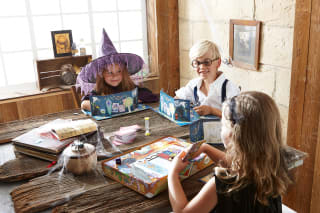 Halloween Spiele | Drei Kinder in Halloween-Kostümen sitzen am Tisch und machen ein Spiel 