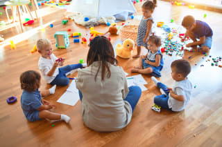 Integrativer Kindergarten | Kinder sitzen mit Erzieherin auf Boden