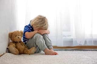 Auf Kinder eingehen | Kind sitzt mit Teddy allein im Zimmer auf einem weißen Teppich