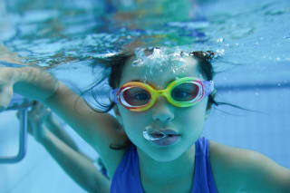 Sicher Planschen | Mädchen mit bunter Schwimmbrille taucht im Wasser.