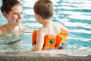  Sicher Planschen | Mutter und Junge mit orangem Schwimmgürtel stehen im Schwimmbecken