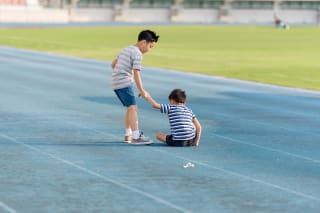 Soziale Kompetenzen | Junge stehend zieht kleinen Jungen an der Hand nach oben