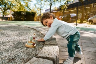 Warum spielen wichtig ist | Kleinkind spielt an einer Steinmauer mit Spielzeug