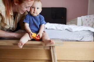 Kinder fördern | Kleinkind sitzt auf Hocker neben dem Bett und hat Auto in der Hand