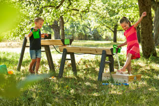 Wasserspiele draußen | Mädchen im roten Kleid spielt mit Jungen an Wasserspielbahn aus Holz