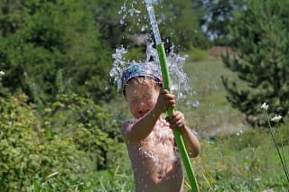 Wasserspiele draußen | Kind spielt mit Gartenschlauch 