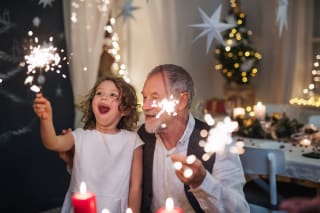 Weihnachten mit Kindern weltweit | Großvater mit kleiner Enkelin zu Weihnachten im Haus, am Tisch sitzend mit Wunderkerzen