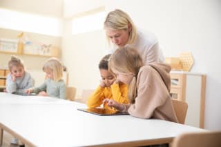 Medienkompetenz | 2 | Image | Tablet als Lerninstrument | Erzieherin schaut über die Schulter von 2 Kinder die mit Tablet lernen 
