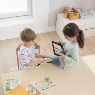Projektidee: E-Book erstellen | Mädchen mit langen braunen Haaren sitzt auf dem Tisch und hält Tablett in der Hand