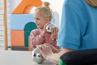 Ein Mädchen sitzt auf dem Boden und spielt mit einem Sinnesball.