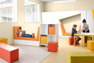Bibliothek | Grid | 2 | Sitzlandschaften | Schüler liegt auf einem Sitzsofa und hört Musik liest dabei ein Buch