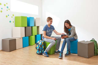  Räume | Schule & Hort |  Schüler und Schülerin sitzen auf grünen, blauen, weißen, braunen Würfeln