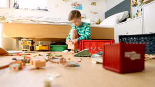 Ein kleiner Junge spielt auf dem Kinderzimmer-Boden. Das Spielzeug ist über den ganzen Boden verteilt.