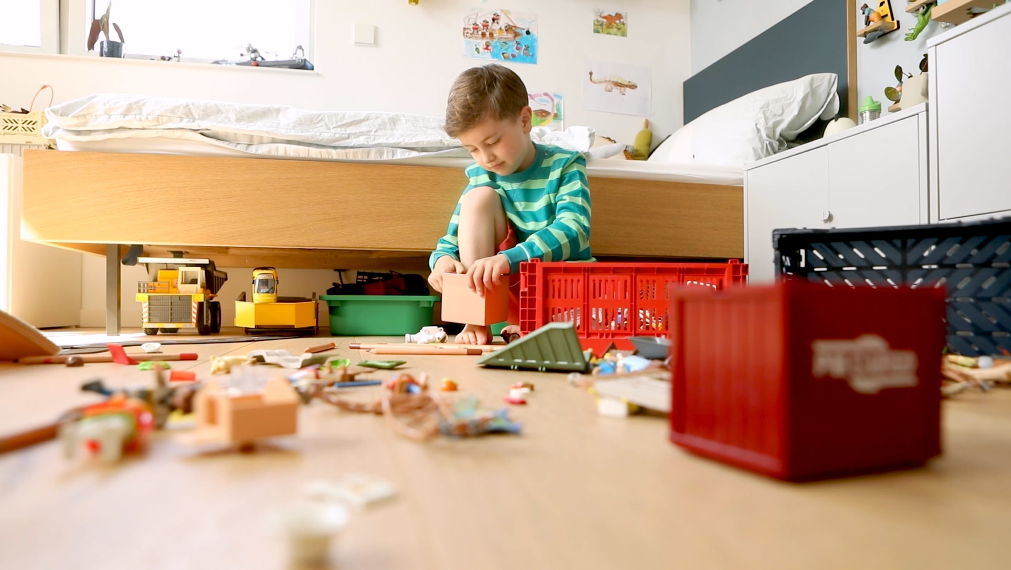 Ein kleiner Junge spielt auf dem Kinderzimmer-Boden. Das Spielzeug ist über den ganzen Boden verteilt.