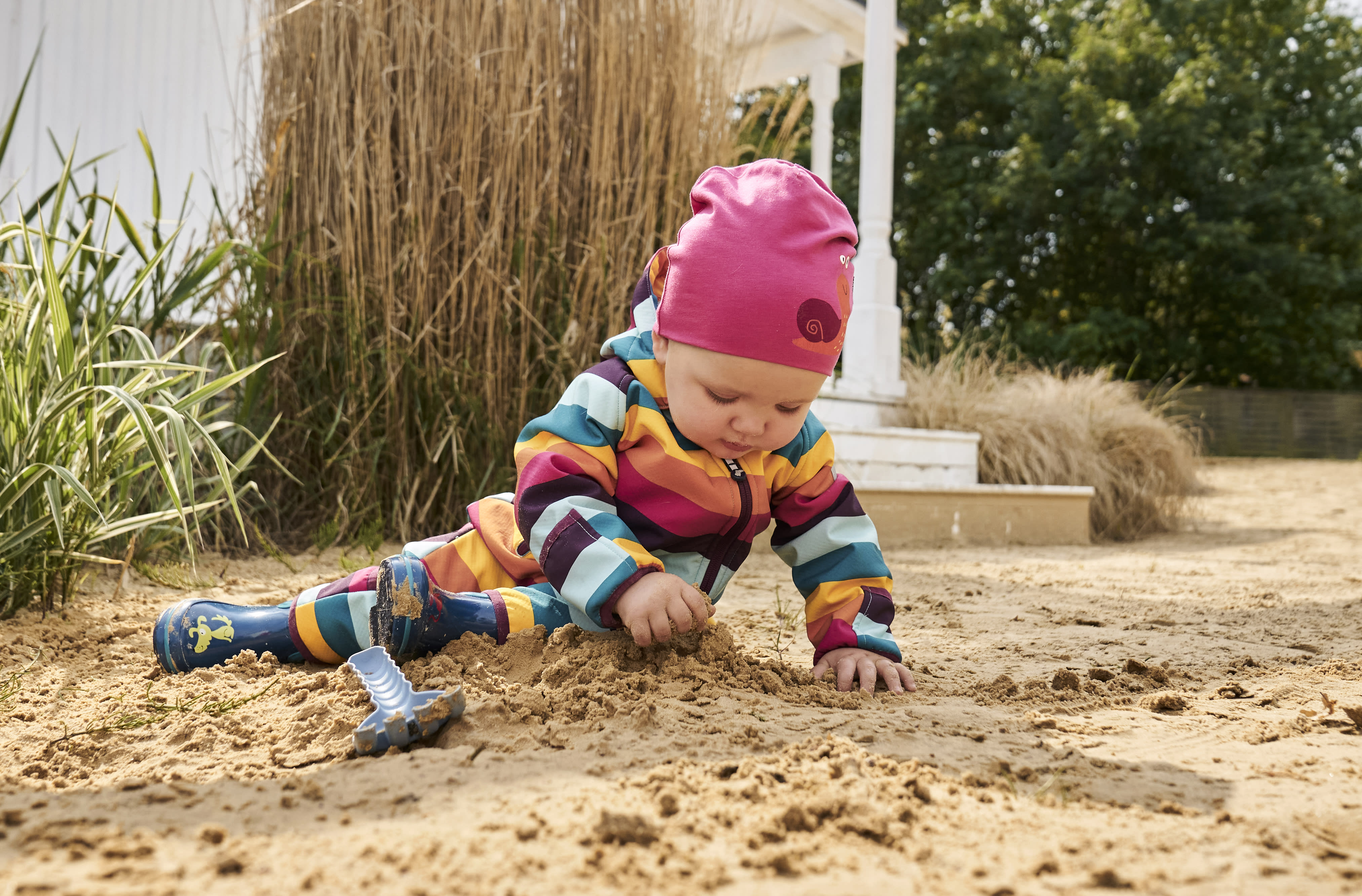  Spiele selber machen | Baby mit bunt geringeltem Softshellanzug spielt draußen im Sand
