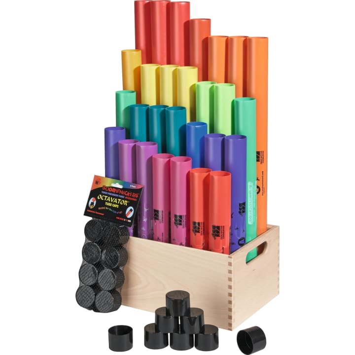 Eine Holzkiste enthält bunte Boomwhackers-Röhren aus Plastik, die nach Größe und Farbe geordnet sind. Schwarze Plastikkappen, Octavators genannt, sind vor der Kiste verstreut und ein beschriftetes Octavator-Set ist darin verstaut.