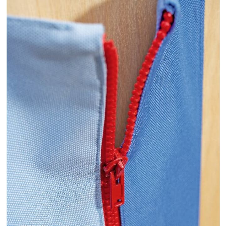 Nahaufnahme eines roten Reißverschlusses, der zwischen zwei blauen Stoffstücken teilweise geöffnet wurde, wobei im Hintergrund ein Teil einer hellbraunen Holzoberfläche zu sehen ist.