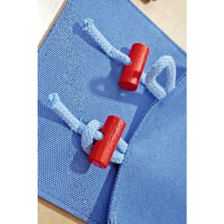 Nahaufnahme von zwei blauen Stoffschlaufen, die mit hellblauen Seilen und roten zylindrischen Holzknebeln auf einer blauen Stofffläche befestigt sind.