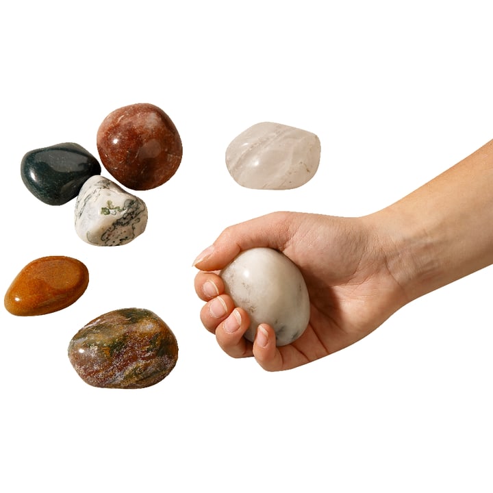 Eine Hand, die einen glatten, ovalen weißen Stein neben fünf anderen polierten Steinen mit unterschiedlichen Farben und Mustern hält, die alle auf einem weißen Hintergrund dargestellt sind.