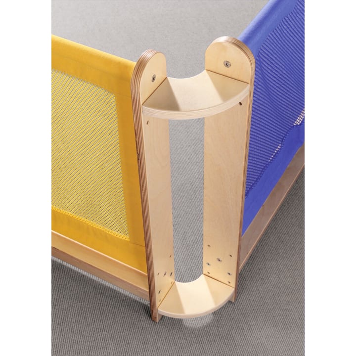 Eine hölzerne Eckverbindung verbindet eine gelbe und eine blaue Maschendrahtbarriere, die beide auf einem grauen Teppichboden stehen. Die Barrieren scheinen eine Trennwand oder einen Sicherheitszaun zu bilden.