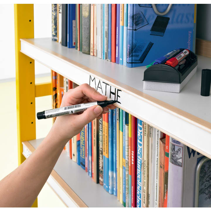 Eine Person schreibt mit einem schwarzen Marker "MATHE" auf den weißen Rand eines mit Büchern gefüllten Bücherregals, in einem Halter auf dem Regal darüber befinden sich Marker und ein Radiergummi.
