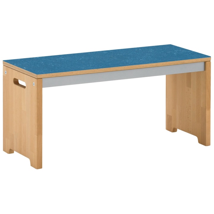 Eine Holzbank mit einer blauen rechteckigen Sitzfläche, hellen Holzbeinen und ausgeschnittenen Griffen an den Seiten. Die Bank hat ein einfaches, modernes Design und ein robustes Aussehen.
