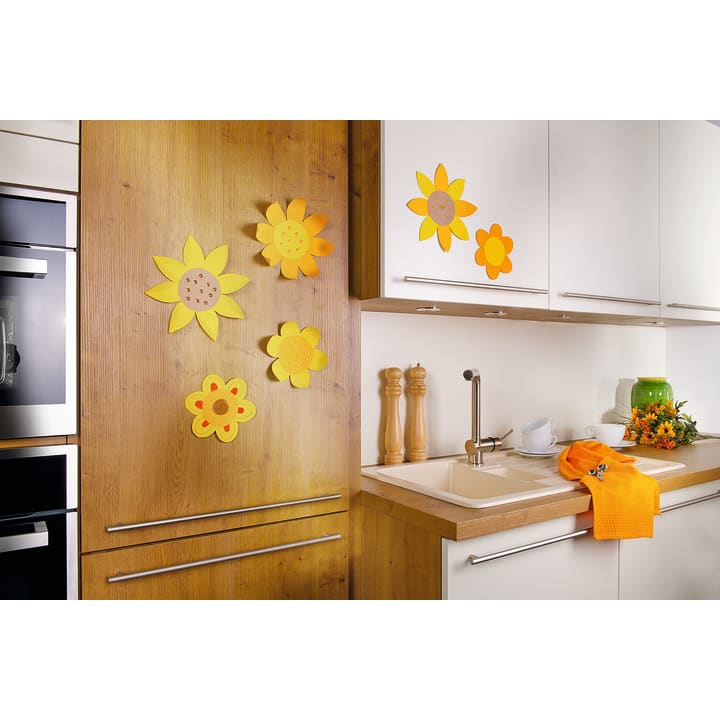 Eine moderne Küche mit weißen und hölzernen Schränken, dekoriert mit gelben und orangefarbenen Papierblumen. Es gibt zwei Tassen und Untertassen, Salz- und Pfeffermühlen und ein orangefarbenes Handtuch neben dem Waschbecken.