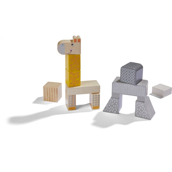 Holzspielzeugklötze sind so angeordnet, dass sie auf der linken Seite eine Giraffe und auf der rechten Seite eine geometrische Struktur bilden, mit einigen losen Klötzen in der Nähe, die alle Schatten auf einen weißen Hintergrund werfen.