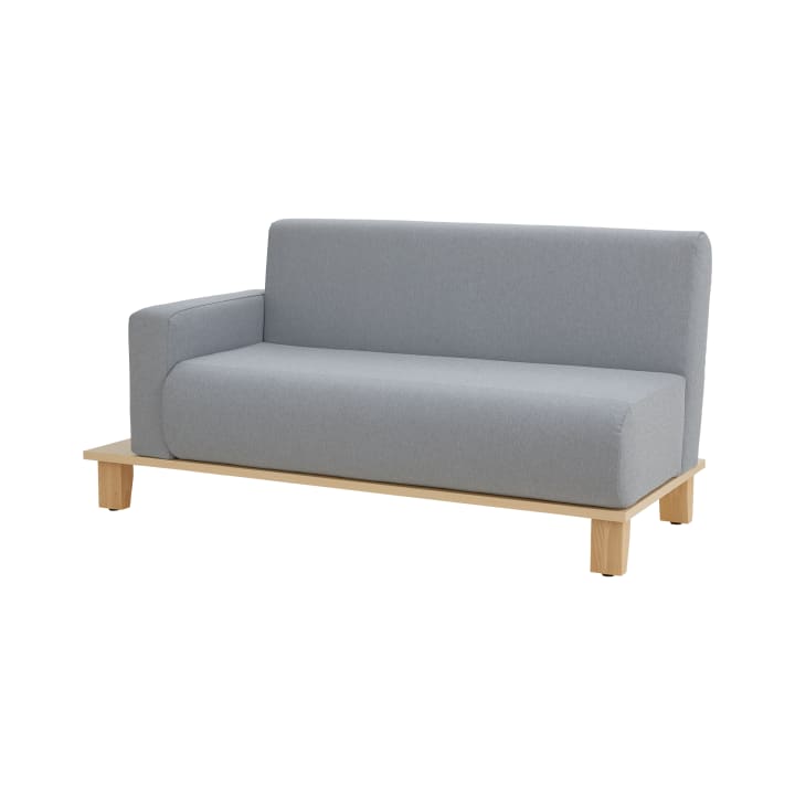 Ein modernes Sofa mit hellgrauer Polsterung, einer einzelnen Armlehne auf der linken Seite und einem Sockel und Beinen aus hellem Holz vor einem schlichten weißen Hintergrund.