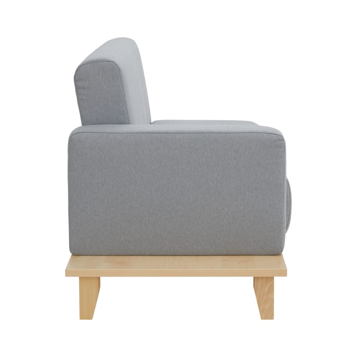 Seitenansicht eines modernen Sofas mit hellgrauem Bezug und rechteckiger Form, auf einem hellen Holzsockel mit vier Beinen, vor einem schlichten weißen Hintergrund.