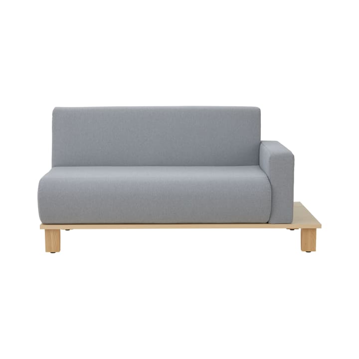Ein modernes, hellgraues Zweisitzer-Sofa mit niedrigem Holzsockel und einer einzelnen Armlehne auf der rechten Seite, vor einem schlichten weißen Hintergrund.