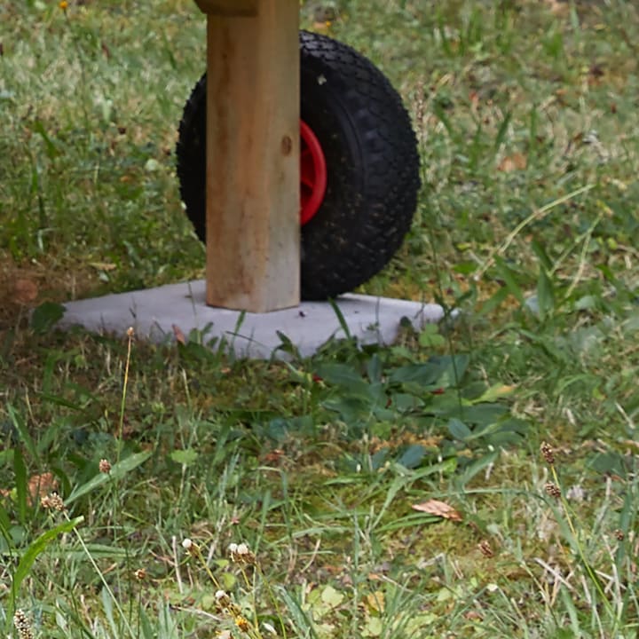 Nahaufnahme eines einzelnen schwarzen Rades mit roter Mitte, das an einem Holzpfosten befestigt ist, der auf einem Betonpflaster inmitten von Gras und kleinen Pflanzen steht.