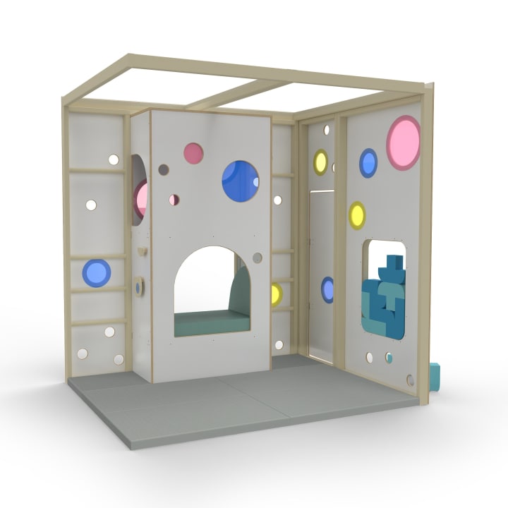 Ein Spielgerät für Kinder im Innenbereich mit weißen Wänden mit unterschiedlich großen runden Ausschnitten in Blau, Rosa und Gelb, einem kleinen Torbogen und Regalen auf der linken Seite. Der Boden ist grau und die Struktur ist nach oben hin offen.
