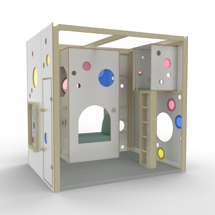 Ein modulares Indoor-Spielhaus mit weißen Paneelen, Naturholzrahmen und kreisförmigen Ausschnitten in verschiedenen Größen und Farben. Es verfügt über einen Loftbereich mit einer Leiter und einer eingebauten Bank darunter, die auf einem grauen Boden steht.