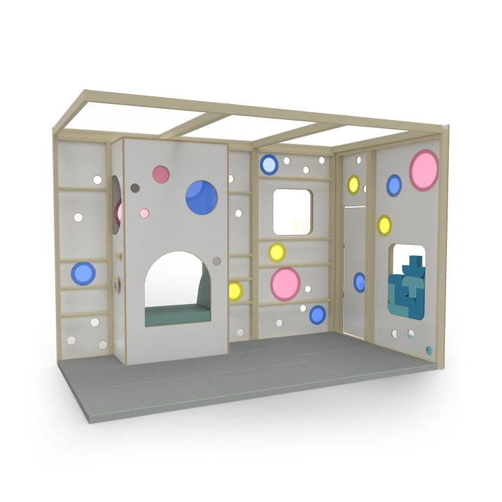 Eine Indoor-Spielstruktur für Kinder mit weißen Wänden, farbenfrohen kreisförmigen Ausschnitten in Rosa, Blau und Gelb, einer Tür, Fenstern und einem grauen Bodenbelag, die zum Klettern und fantasievollen Spielen einlädt.