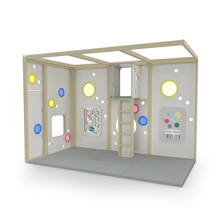 Eine modulare Spielstruktur für den Innenbereich mit hellem Holzrahmen, grauen Wänden mit bunten runden Fenstern, einem Aktivitätspaneel, einer Leiter, einem Loftbereich und einem gepolsterten Boden.