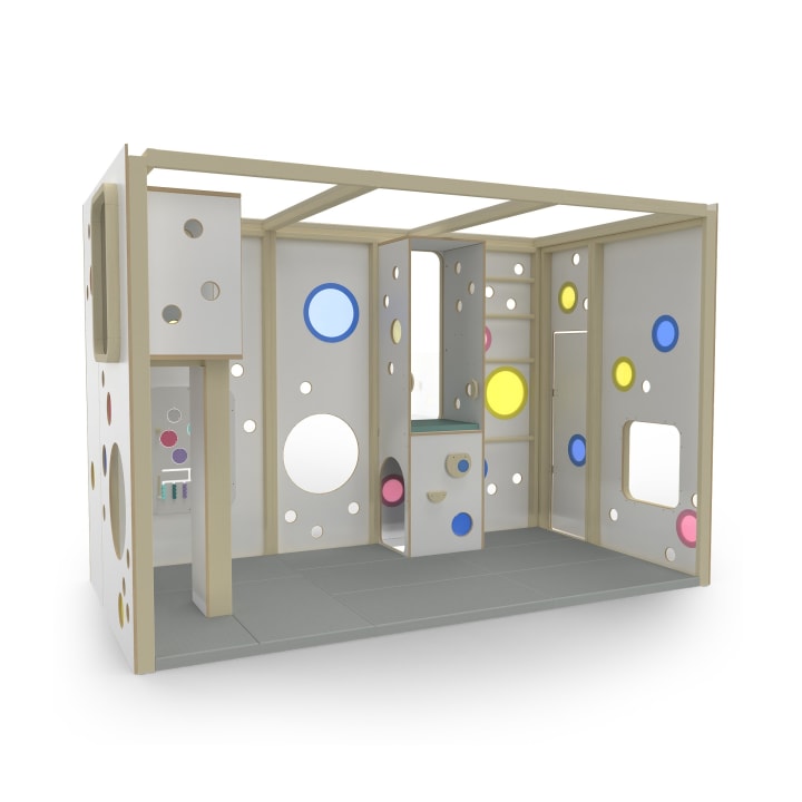 Eine moderne Spielstruktur für den Innenbereich mit weißen und beigen Paneelen, die runde und quadratische Aussparungen in verschiedenen Farben und eingebaute Regale aufweisen und auf einer grauen Bodenmatte stehen.