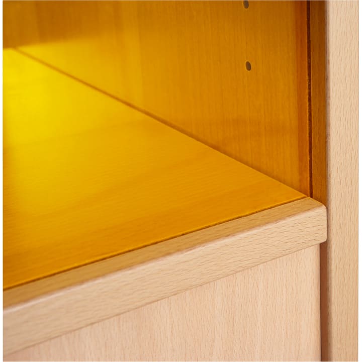 Nahaufnahme der Innenecke eines hellen Holzschranks mit einem gelb getönten Glasboden und einer Rückwand. An der Seitenwand sind zwei kleine Löcher für Regalstützen zu sehen.