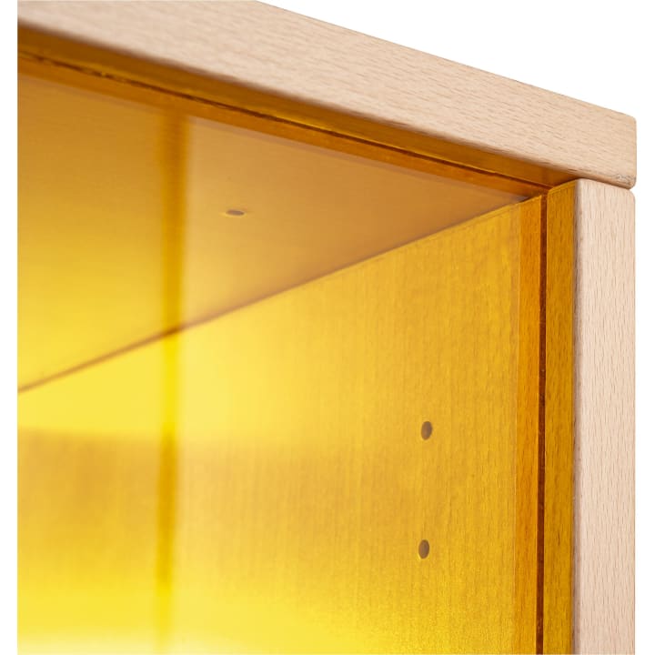 Nahaufnahme der Ecke einer Holzstruktur mit einer durchscheinenden gelben Platte im Inneren. Das Holz hat eine helle Oberfläche, und die gelbe Platte ist mit sichtbaren kleinen Löchern befestigt. Der Hintergrund ist weiß.