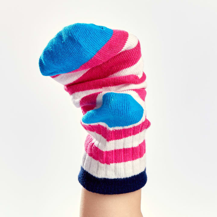 Eine Hand, die eine bunte Sockenpuppe mit rosa, weißen und blauen Streifen trägt, wird aufrecht vor einem schlichten weißen Hintergrund gehalten.