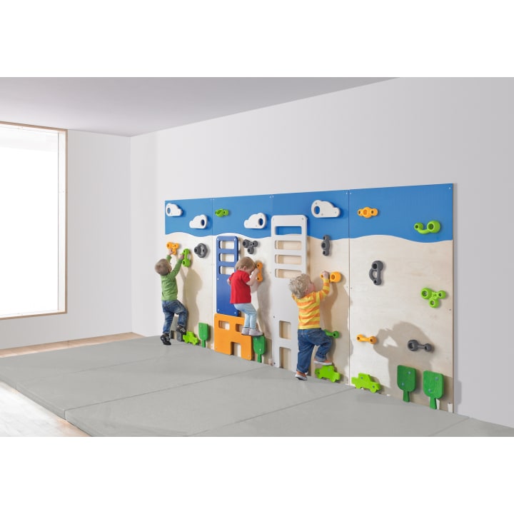 Drei kleine Kinder klettern an einer bunten Indoor-Kletterwand mit verschiedenen Griffen und Formen. Der Raum hat weiße Wände, ein großes Fenster und einen gepolsterten Boden für die Sicherheit.