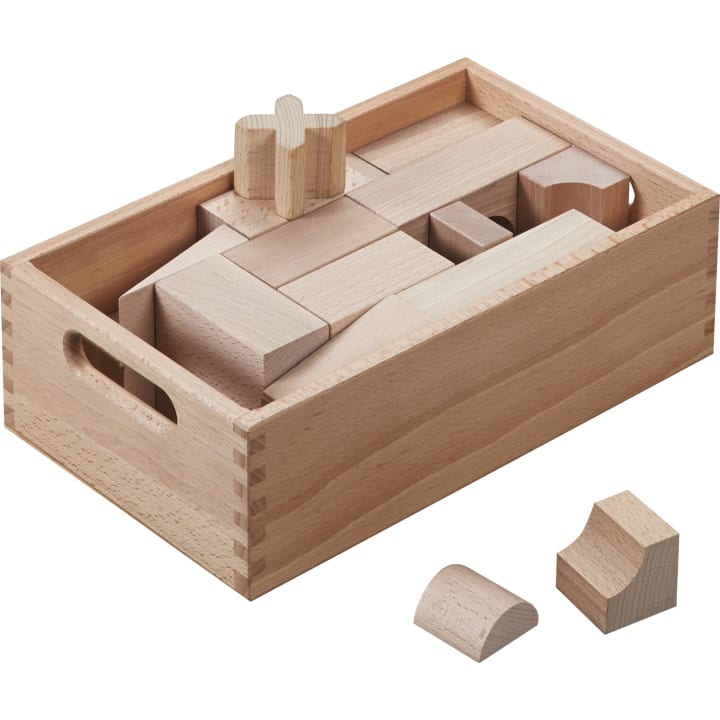 Eine Holzkiste mit Griffen enthält verschiedene Holzbausteine in unterschiedlichen Formen und Größen. Zwei gebogene Klötze sind außerhalb der Kiste im Vordergrund platziert.