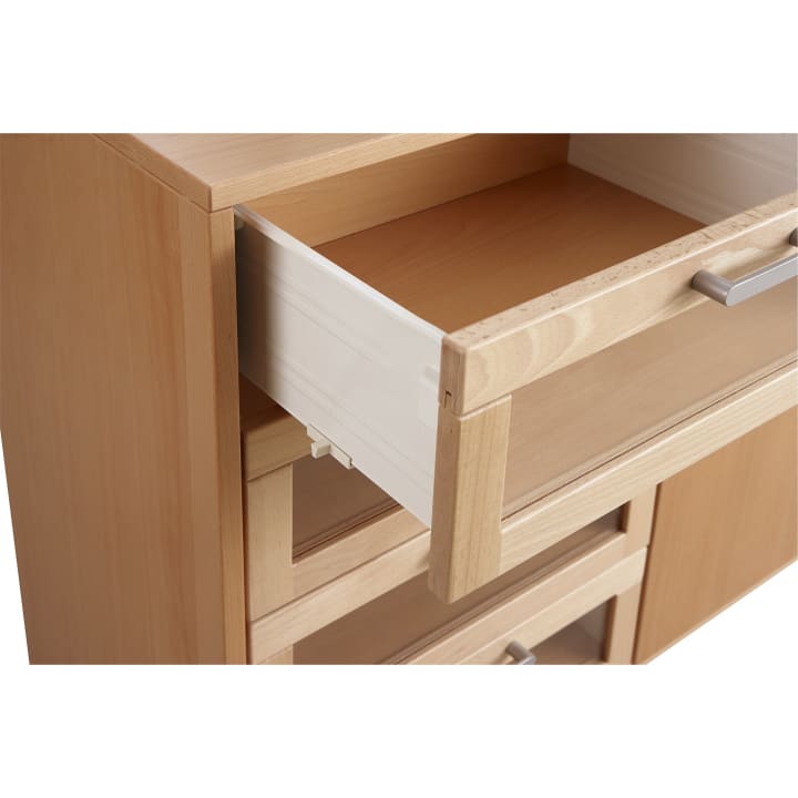 Nahaufnahme eines hellen Holzschranks mit Metallgriffen, bei dem eine Schublade teilweise geöffnet und das Innere der Schublade sichtbar ist.