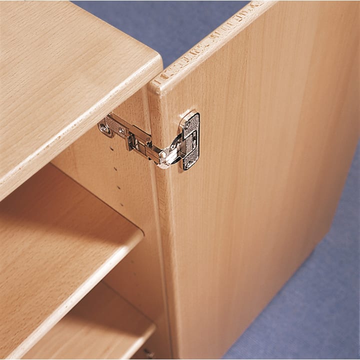 Nahaufnahme eines Schranks aus hellem Holz mit geöffneter Tür, die ein Metallscharnier an der Tür und am Schrankrahmen zeigt. Im Inneren sind Einlegeböden zu sehen, und der Hintergrund ist eine blaue Fläche.