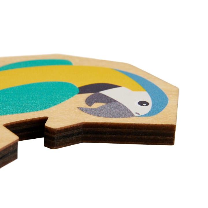 Eine Nahaufnahme eines dicken hölzernen Puzzlestücks mit einer einfachen, bunten Illustration eines Papageis, mit grünen, gelben, schwarzen und weißen Formen auf einem natürlichen Holzhintergrund.