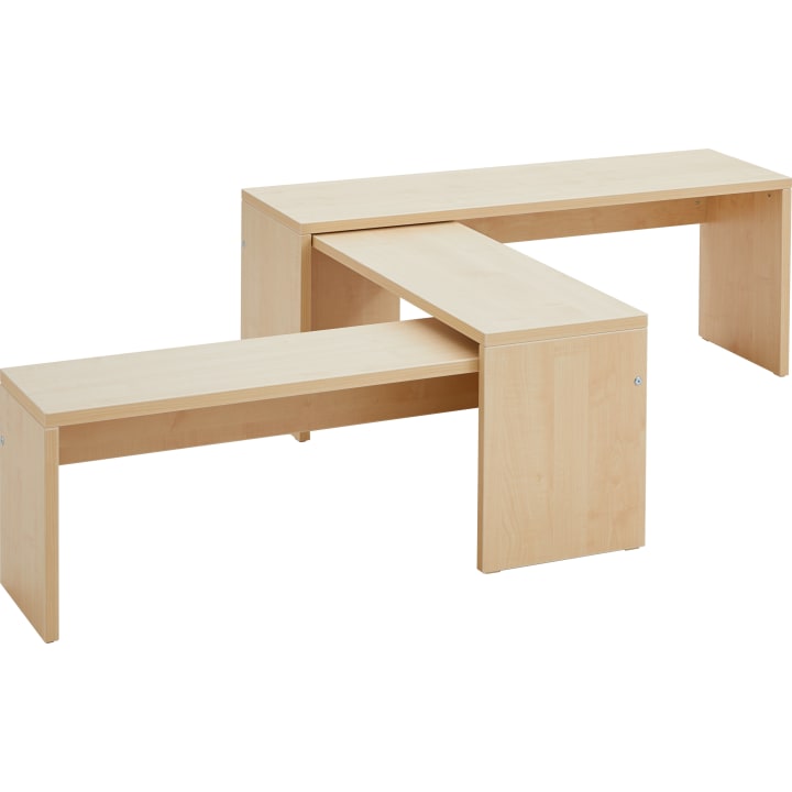 Zwei Bänke aus hellem Holz kreuzen sich in einem rechten Winkel und bilden eine L-Form. Jede Bank hat einfache, rechteckige Beine und eine glatte Oberfläche. Beide Stücke haben sichtbare Metallschrauben an den Ecken.