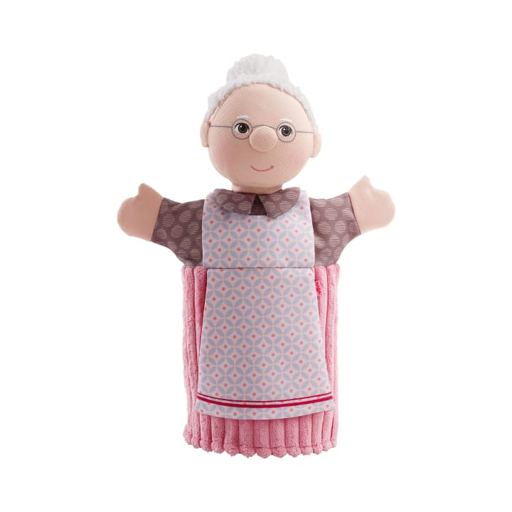 Eine Handpuppe, die wie eine ältere Frau aussieht, mit weißem Haar in einem Dutt, einer Brille, einer gemusterten Bluse und einer rosa-weißen Schürze.