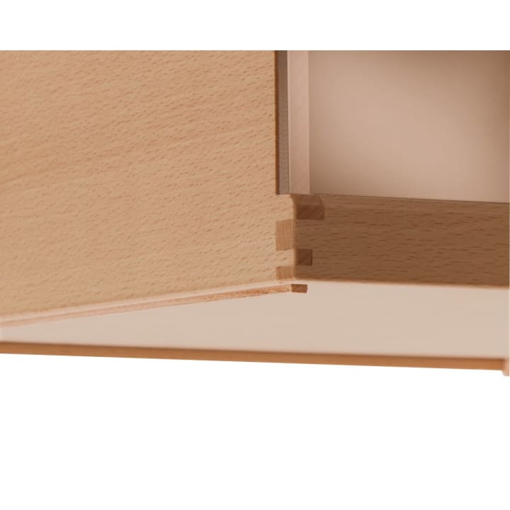 Nahaufnahme einer hölzernen Schubladenecke, die eine Schwalbenschwanzverbindung zeigt, bei der helle Holzplatten präzise ineinandergreifen und eine starke, saubere Verbindung bilden. Der Hintergrund ist schlicht und unscharf.