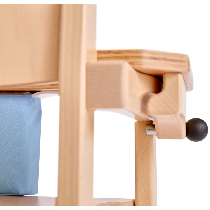 Nahaufnahme eines hellen Holzstuhls mit einer blauen Stofftasche unter der Sitzfläche und einem schwarzen runden Verstellknopf an der Seite.